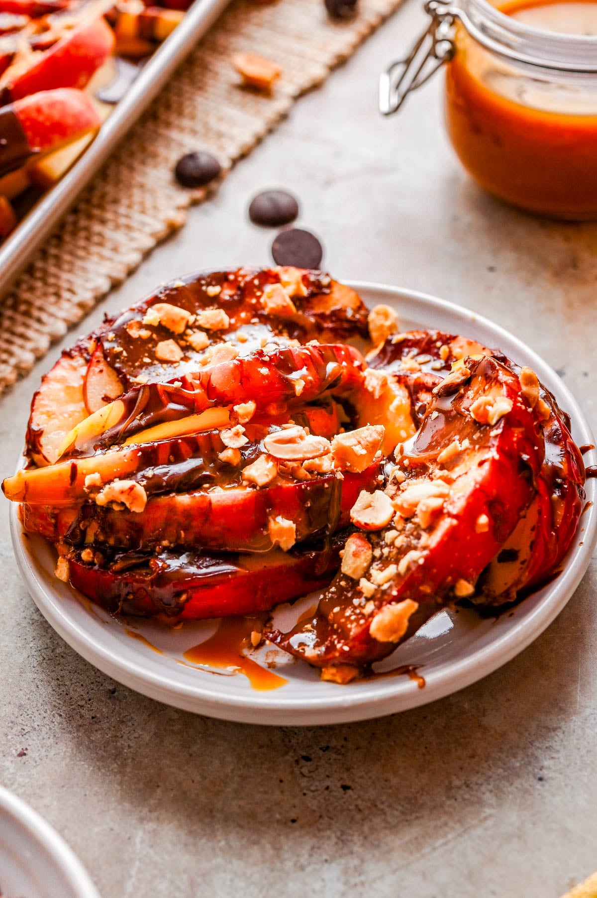 Sliced apples topped with caramel sauce, chocolate drizzle, and chopped nuts arranged on a small white plate.