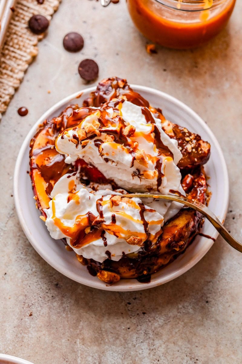 A plate of French toast topped with whipped cream, chocolate sauce, and nuts, with a fork resting on the side.