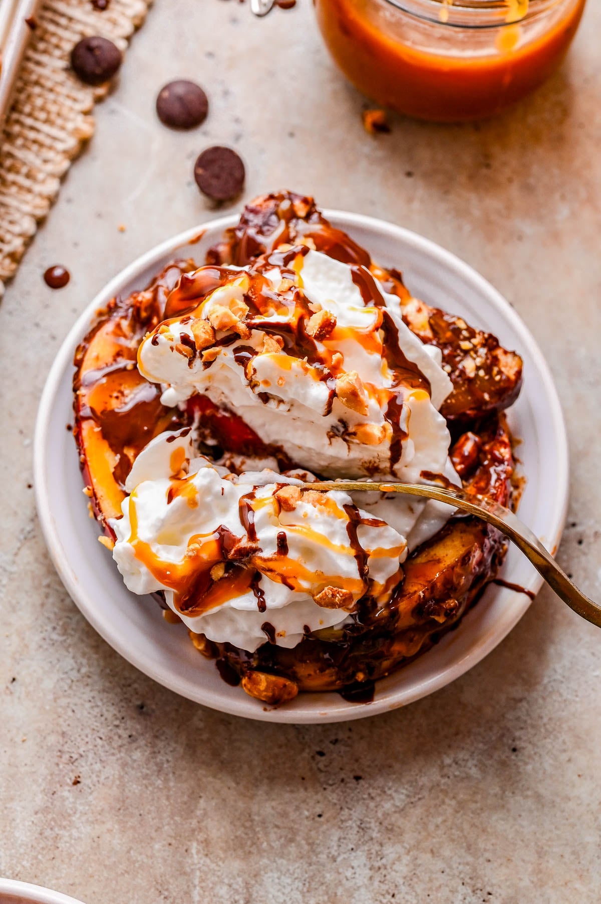 A plate of French toast topped with whipped cream, chocolate sauce, and nuts, with a fork resting on the side.