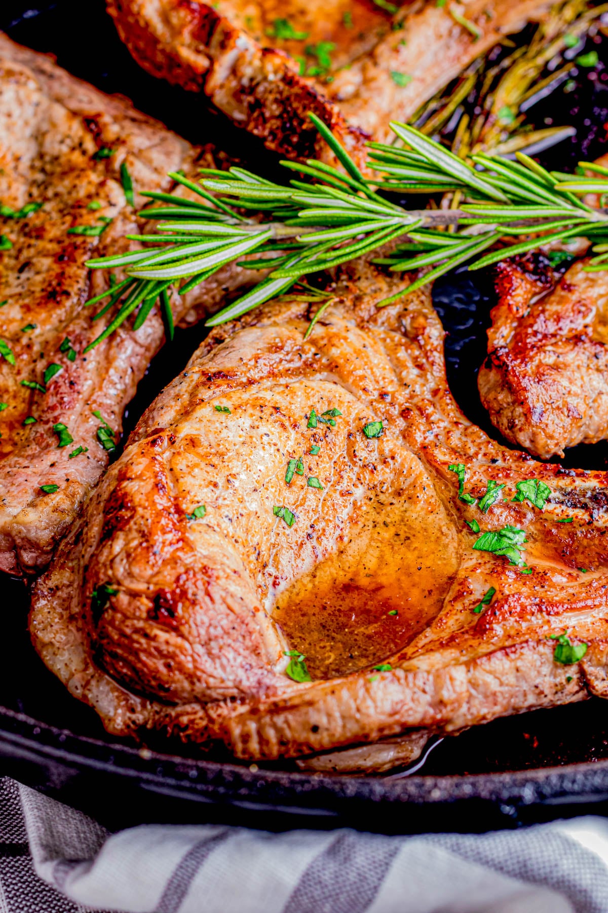 A cooked pork chop garnished with herbs and a sprig of rosemary in a cast iron skillet.