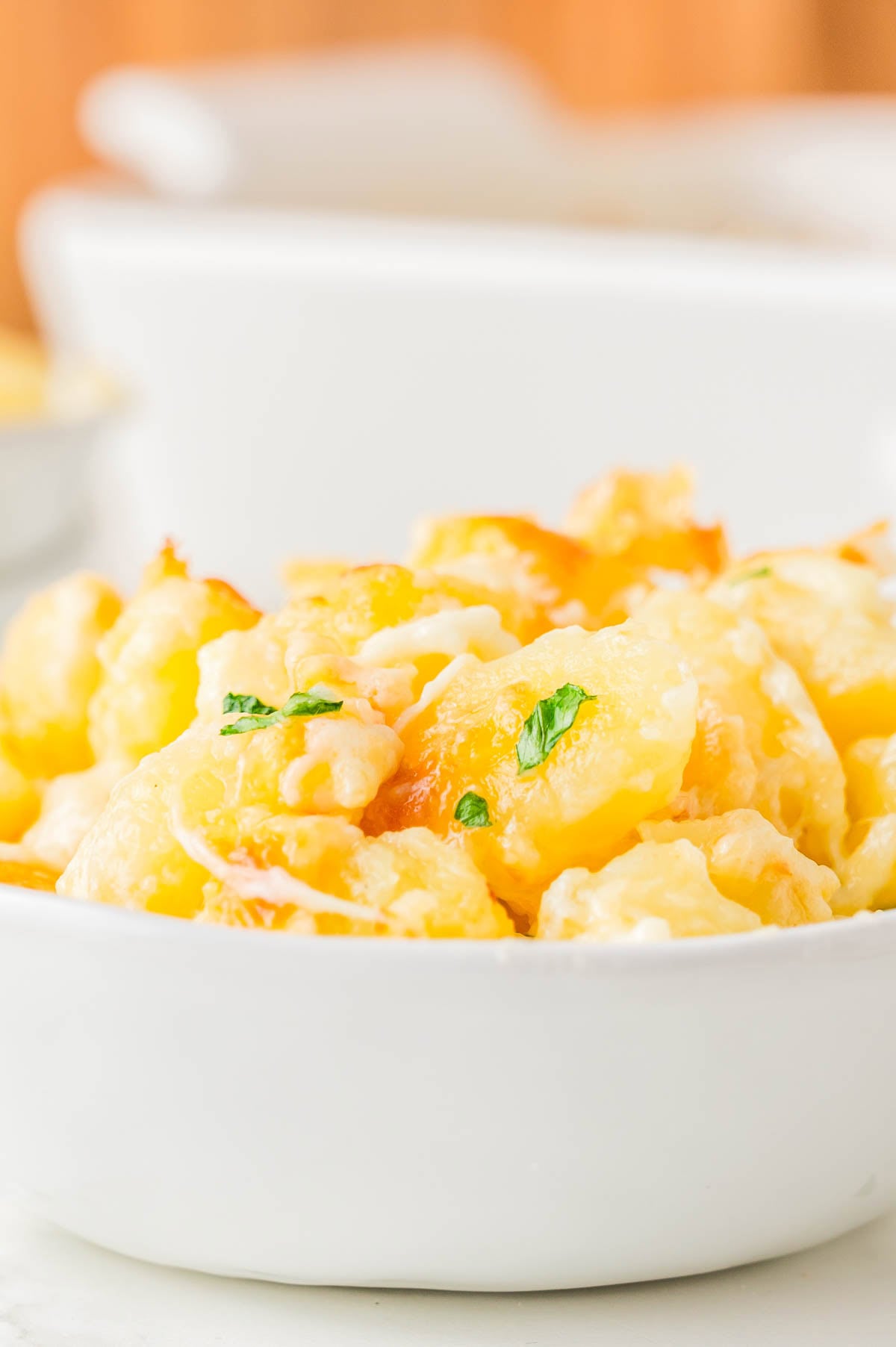 A white bowl filled with baked macaroni and cheese, garnished with a small amount of chopped parsley.