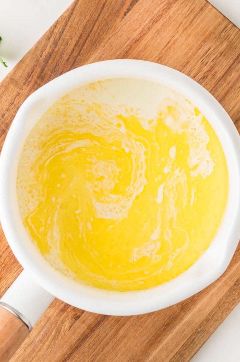 A white saucepan with melted butter and cream swirling together sits on a wooden cutting board.