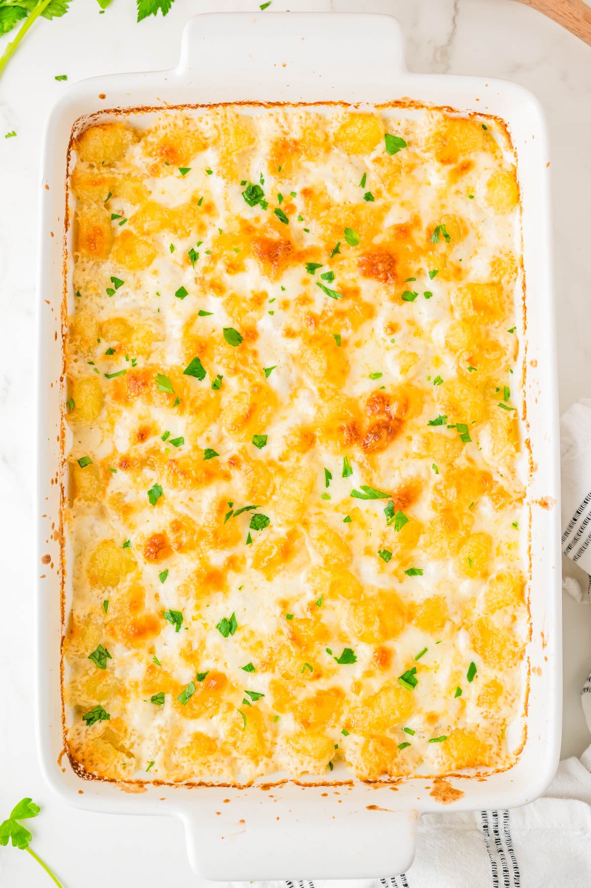 A baked casserole topped with melted cheese and chopped parsley in a white rectangular dish, shown from above.