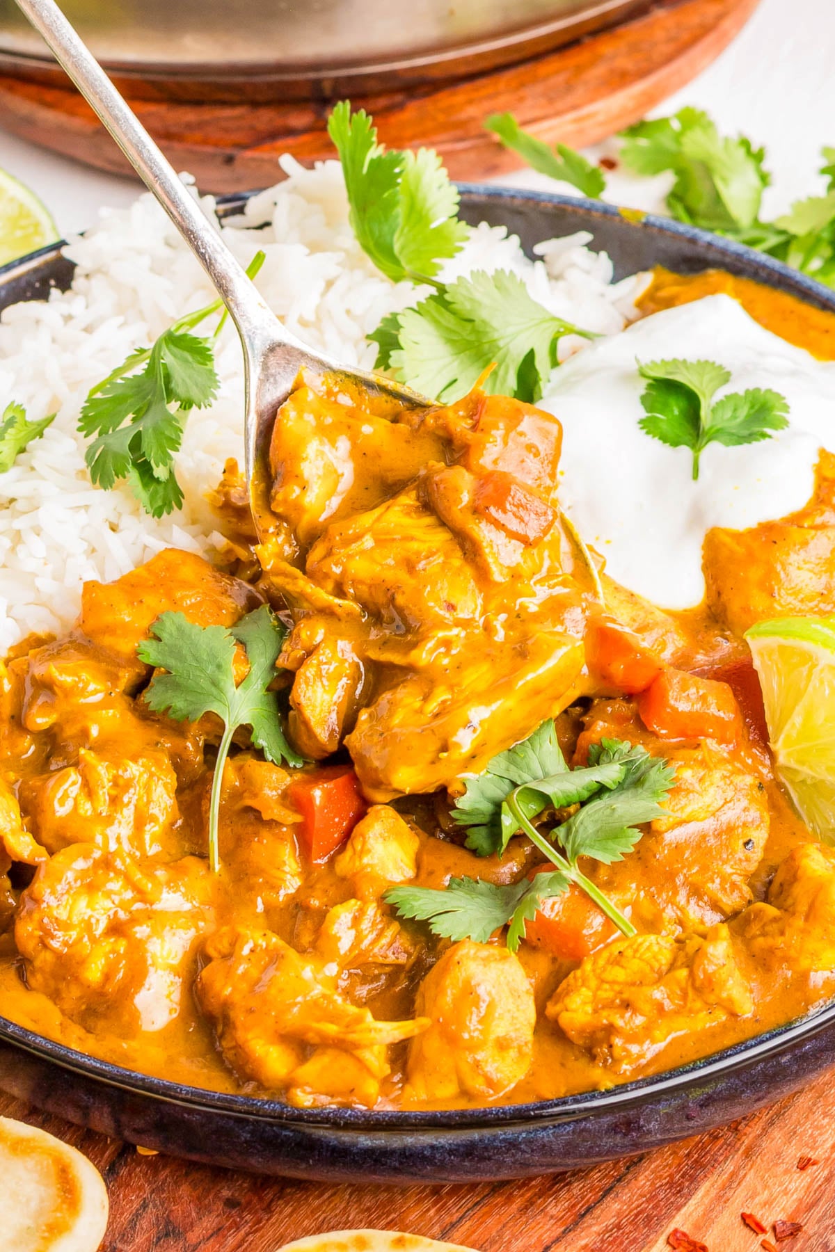Plate of chicken curry with white rice, garnished with cilantro and a lemon wedge, and a spoon lifting a portion of the curry.