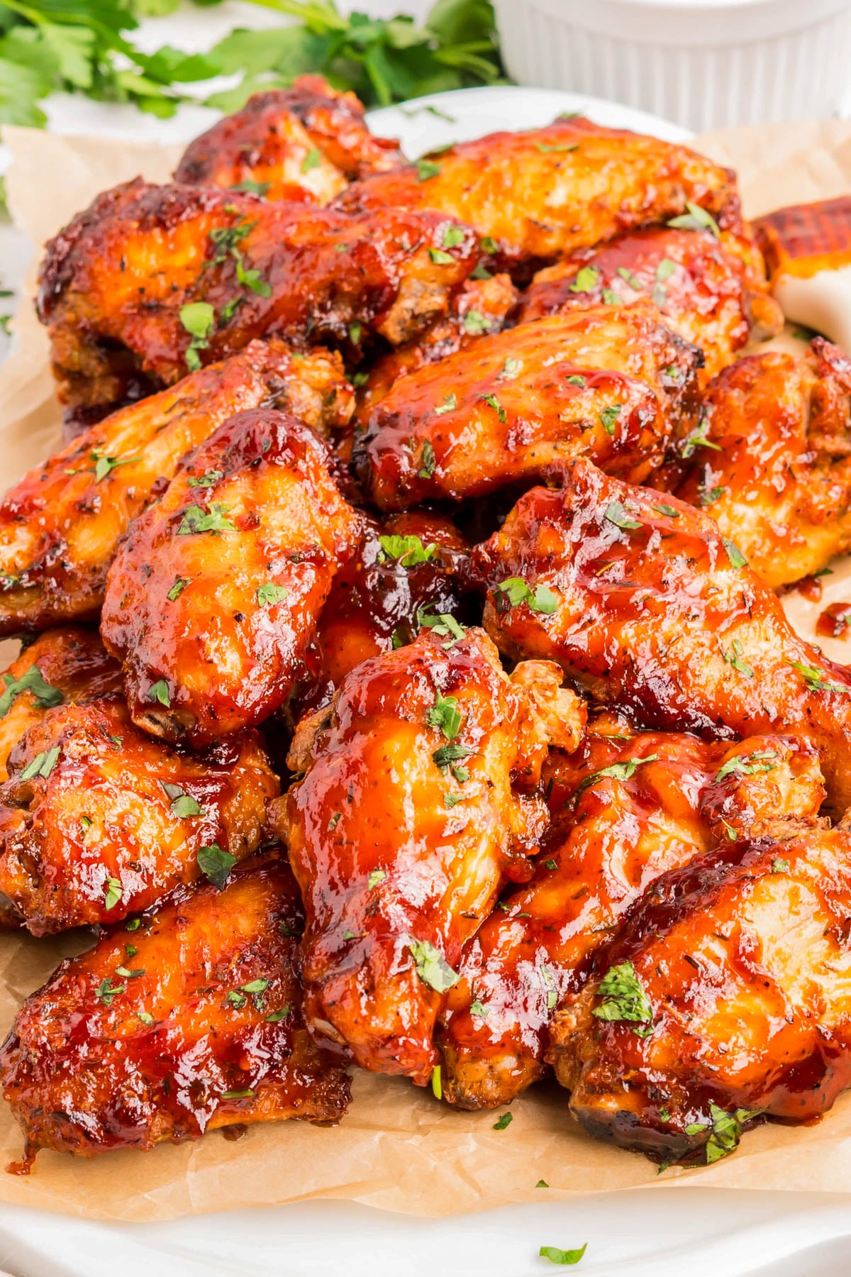 A plate of glazed chicken wings garnished with chopped herbs, served on parchment paper.