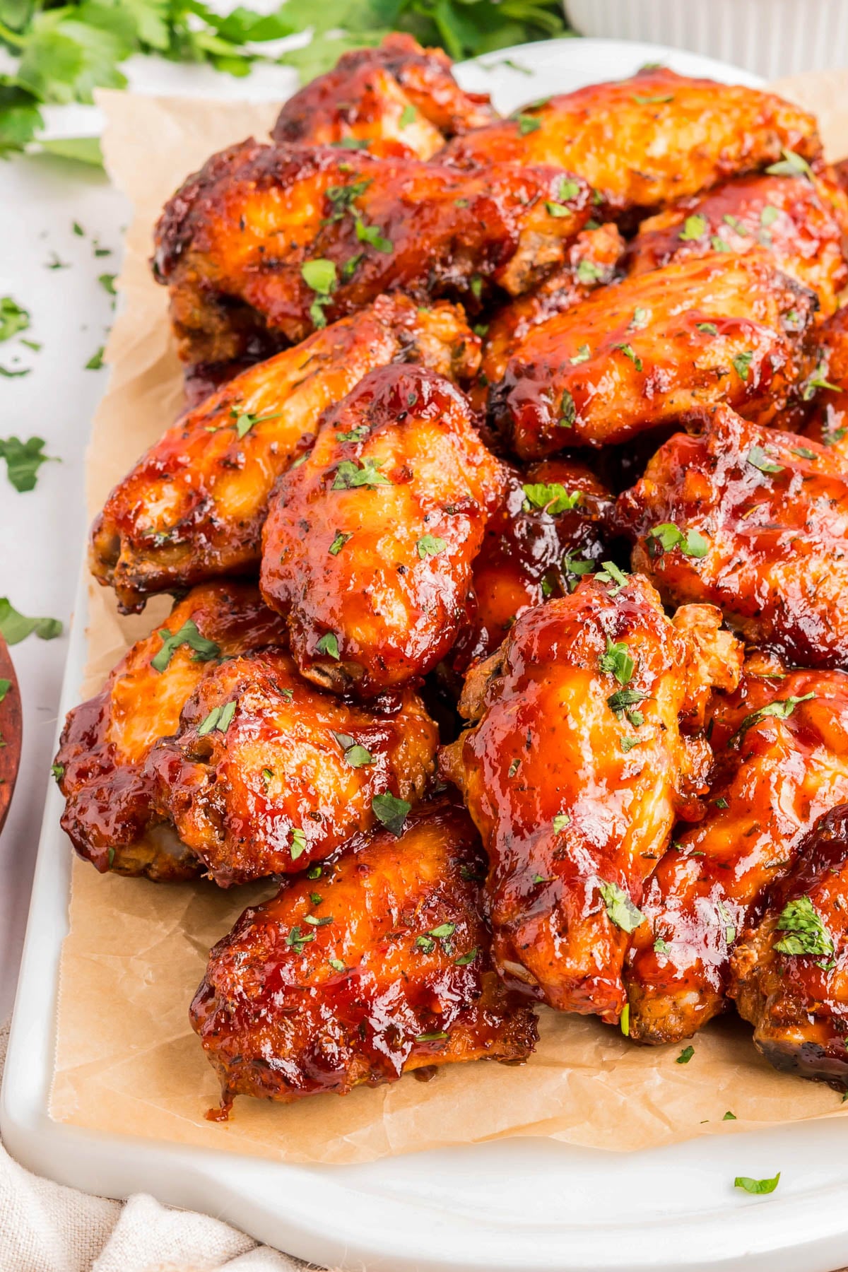 A tray of glazed chicken wings garnished with chopped herbs, arranged on parchment paper.