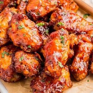 A tray of glazed chicken wings garnished with chopped herbs, placed on parchment paper, with a basting brush in the background.