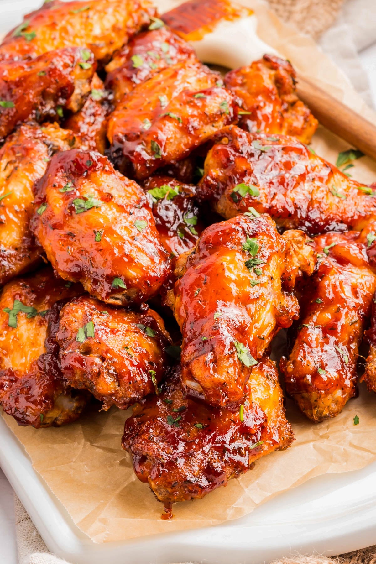 A tray of glazed chicken wings garnished with chopped herbs, placed on parchment paper, with a basting brush in the background.