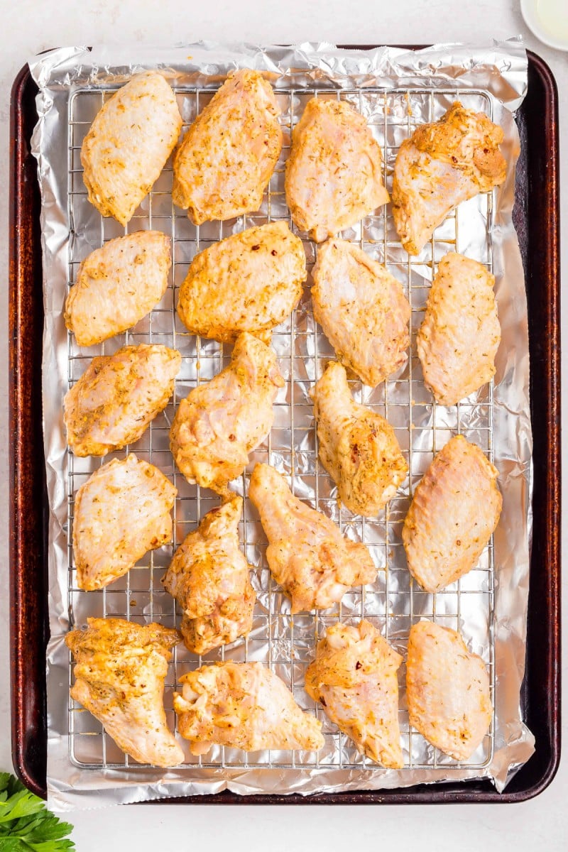 Raw, marinated chicken pieces are arranged on a wire rack over a foil-lined baking sheet, ready for cooking.