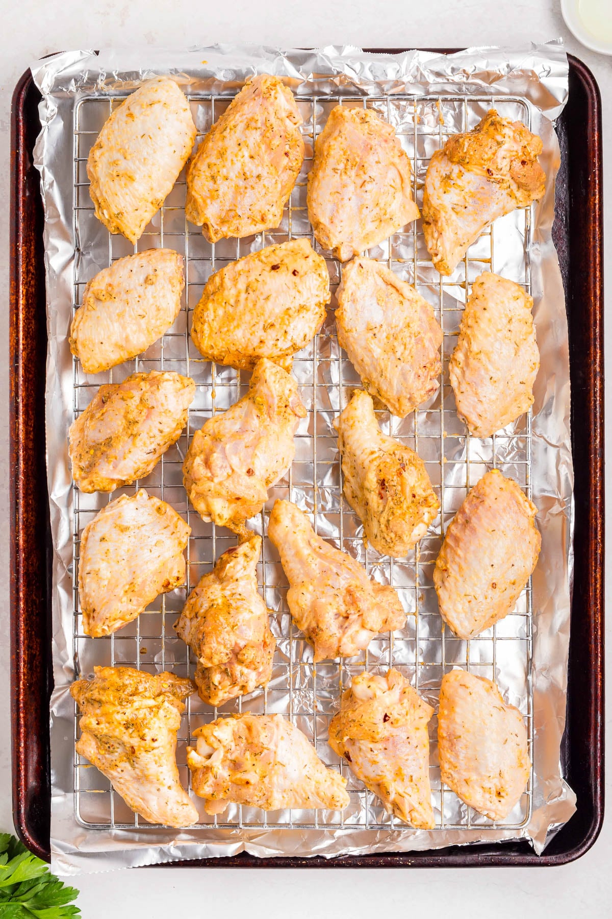 Raw, marinated chicken pieces are arranged on a wire rack over a foil-lined baking sheet, ready for cooking.