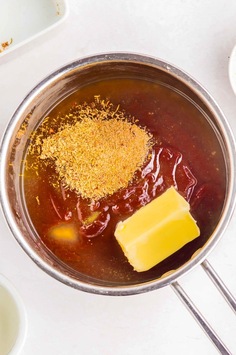 A saucepan contains a block of butter, seasoning, and a thick reddish sauce, possibly for mixing or cooking.