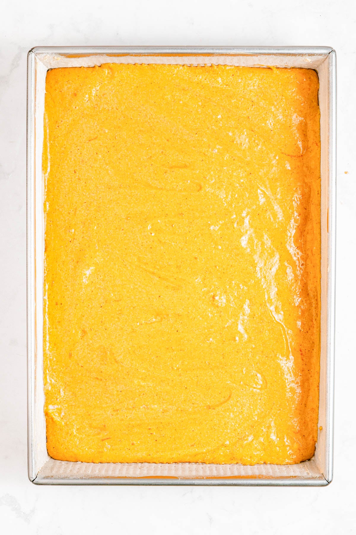 A rectangular metal baking pan filled with a smooth, evenly baked yellow cake with a slightly glossy surface.