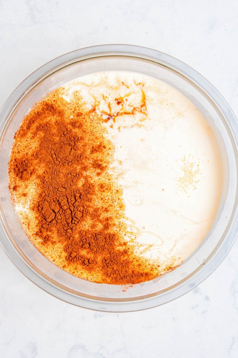 A glass bowl containing a creamy white mixture with ground cinnamon and spices sprinkled on one side, seen from above.