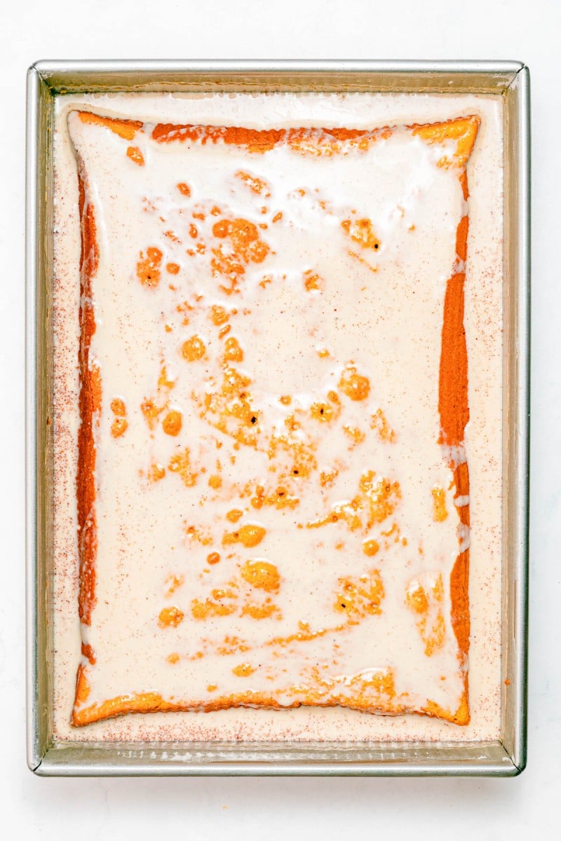 Rectangular baking dish with a yellow cake soaked in a creamy milk mixture, viewed from above on a white background.