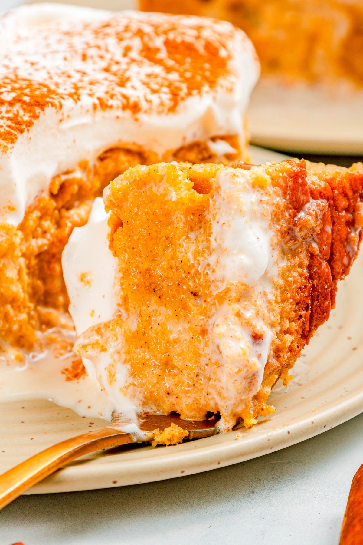 A close-up of a slice of pumpkin pie topped with whipped cream on a plate, with a fork holding a bite-sized piece.
