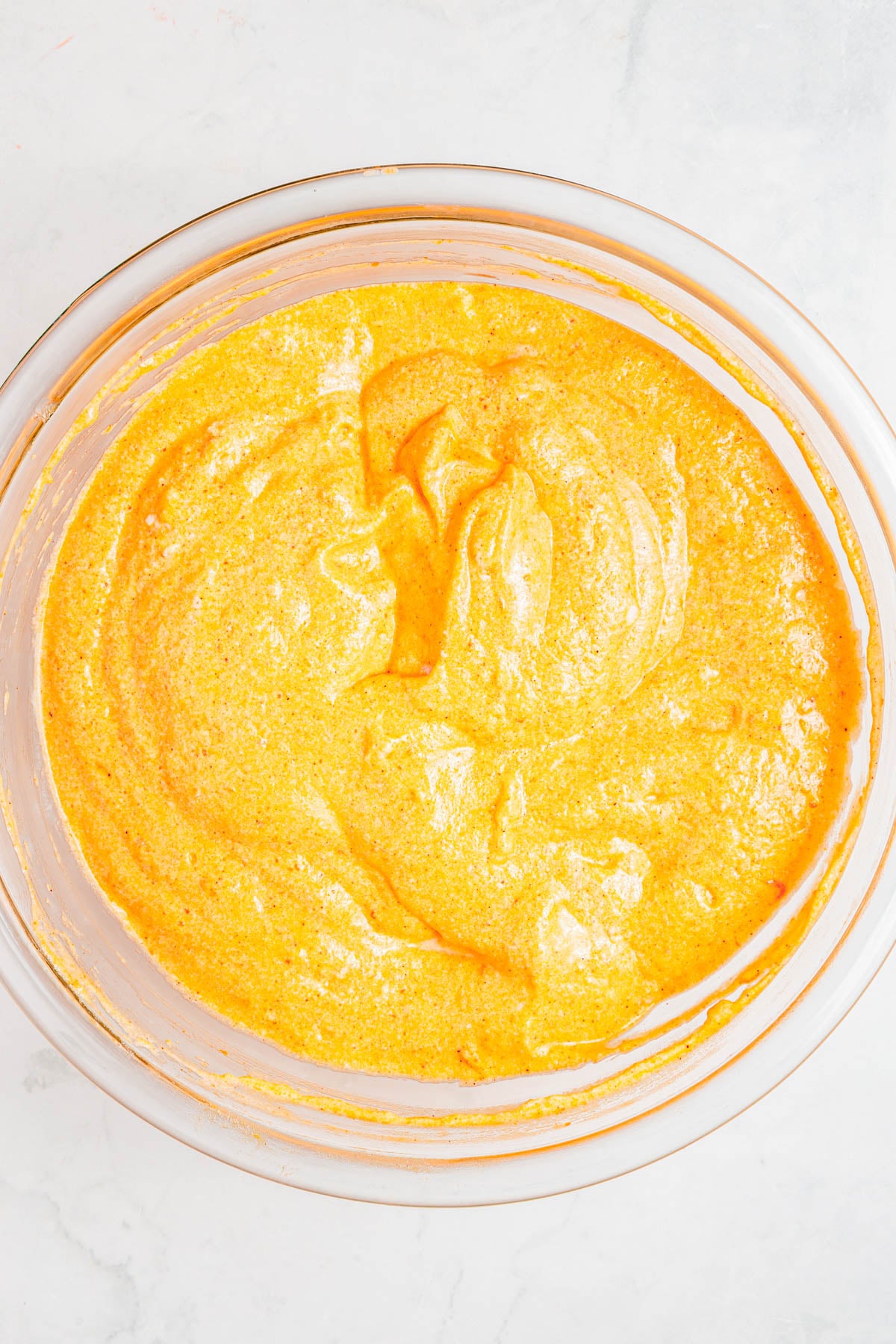 A glass bowl filled with bright yellow, thick batter or mixture, sitting on a light-colored countertop.