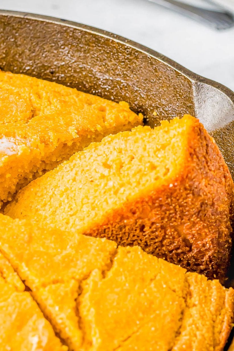 A sliced cornbread in a cast iron skillet, showing a golden brown crust and a moist interior.