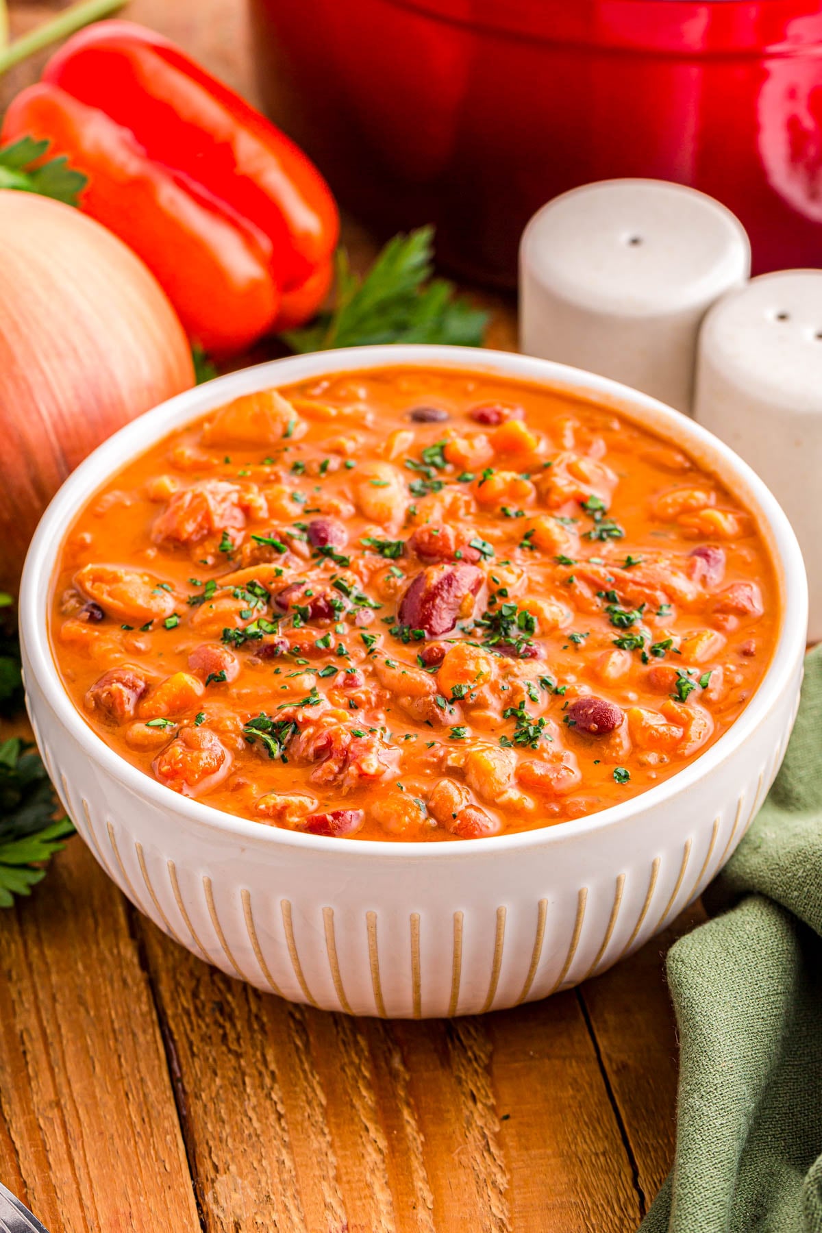 A white bowl of creamy bean chili garnished with fresh herbs, sitting on a wooden table.