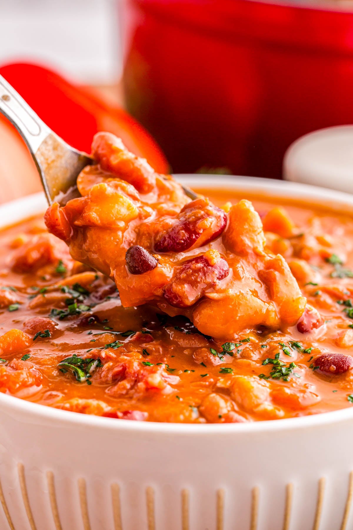 A spoonful of thick, red bean chili being lifted from a bowl.