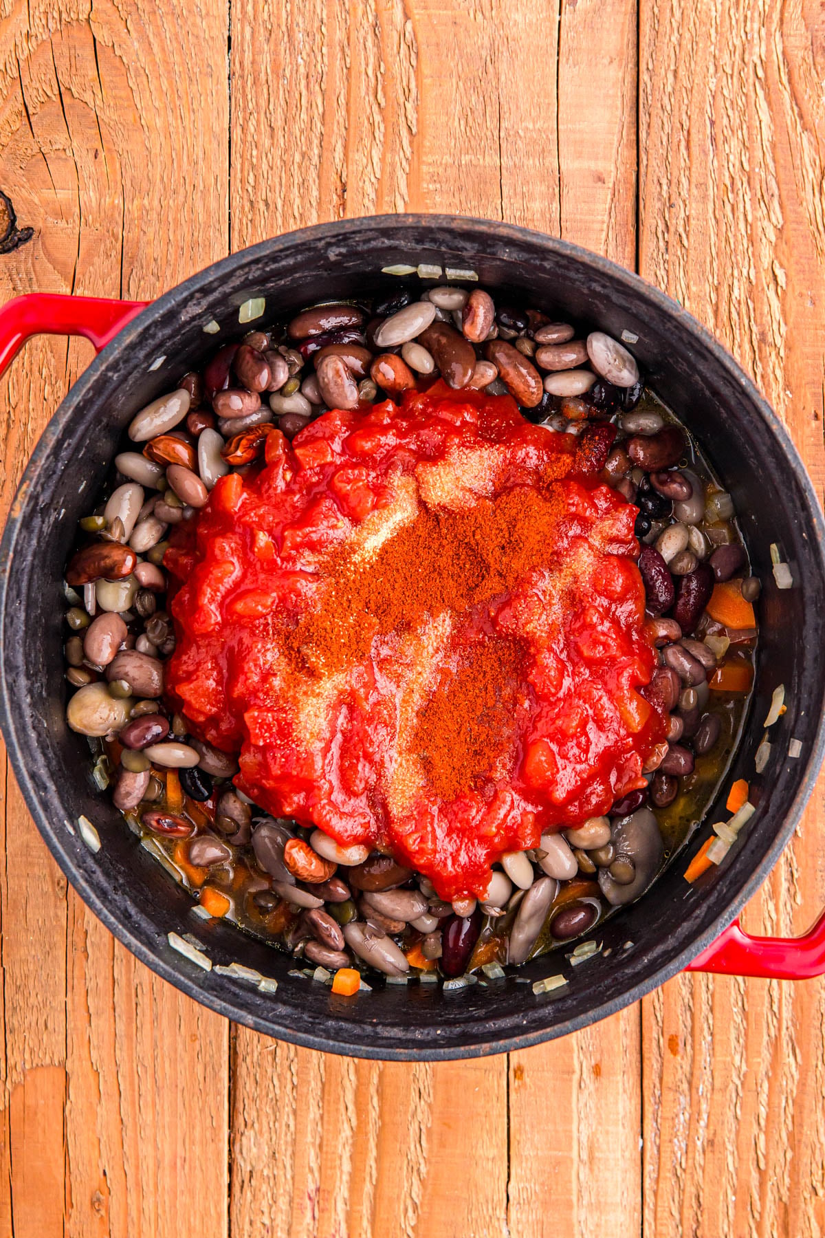 A pot of mixed beans, chopped vegetables, and tomato sauce, seasoned with spices.