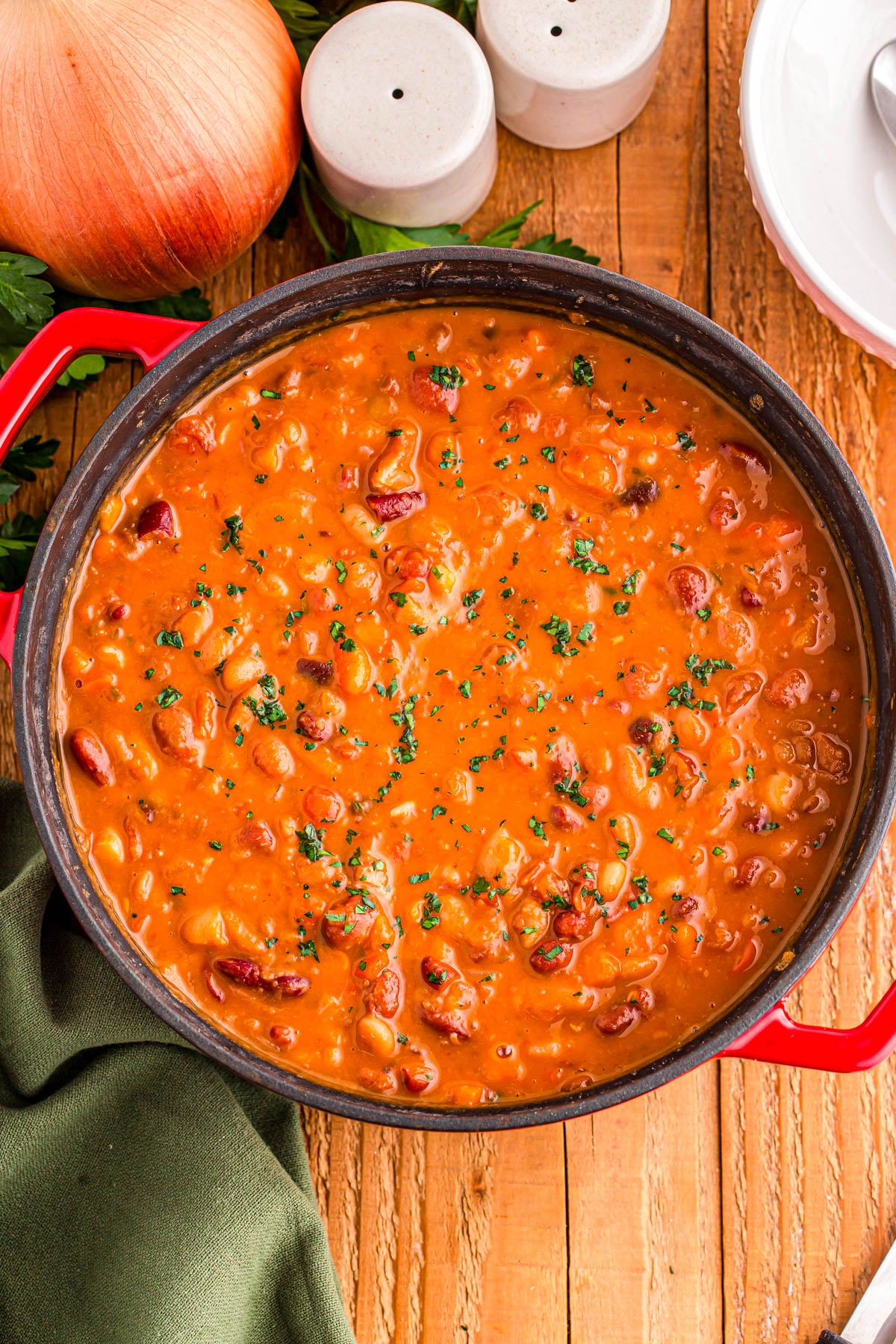 A pot of bean chili garnished with fresh herbs, viewed from above on a wooden surface.