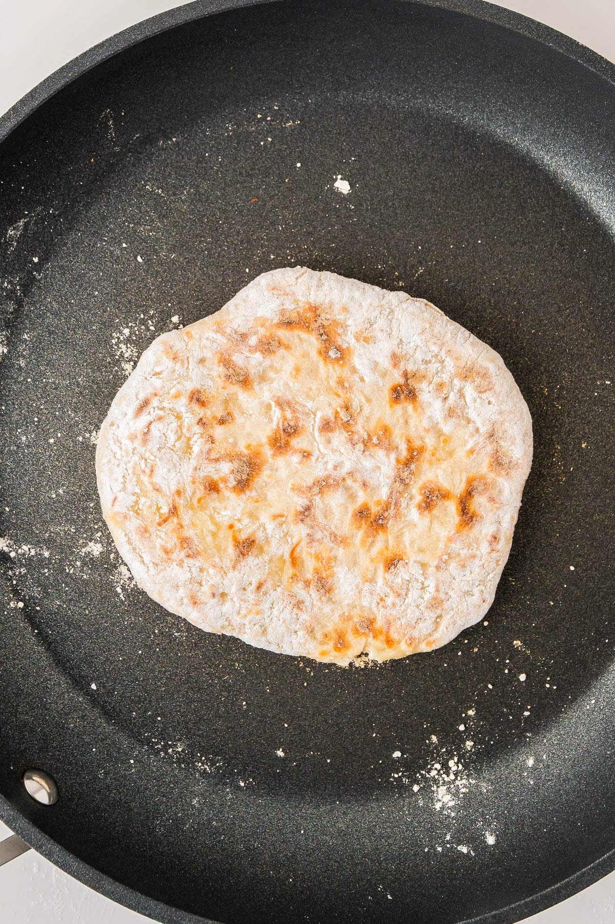 A round flatbread cooking in a frying pan.