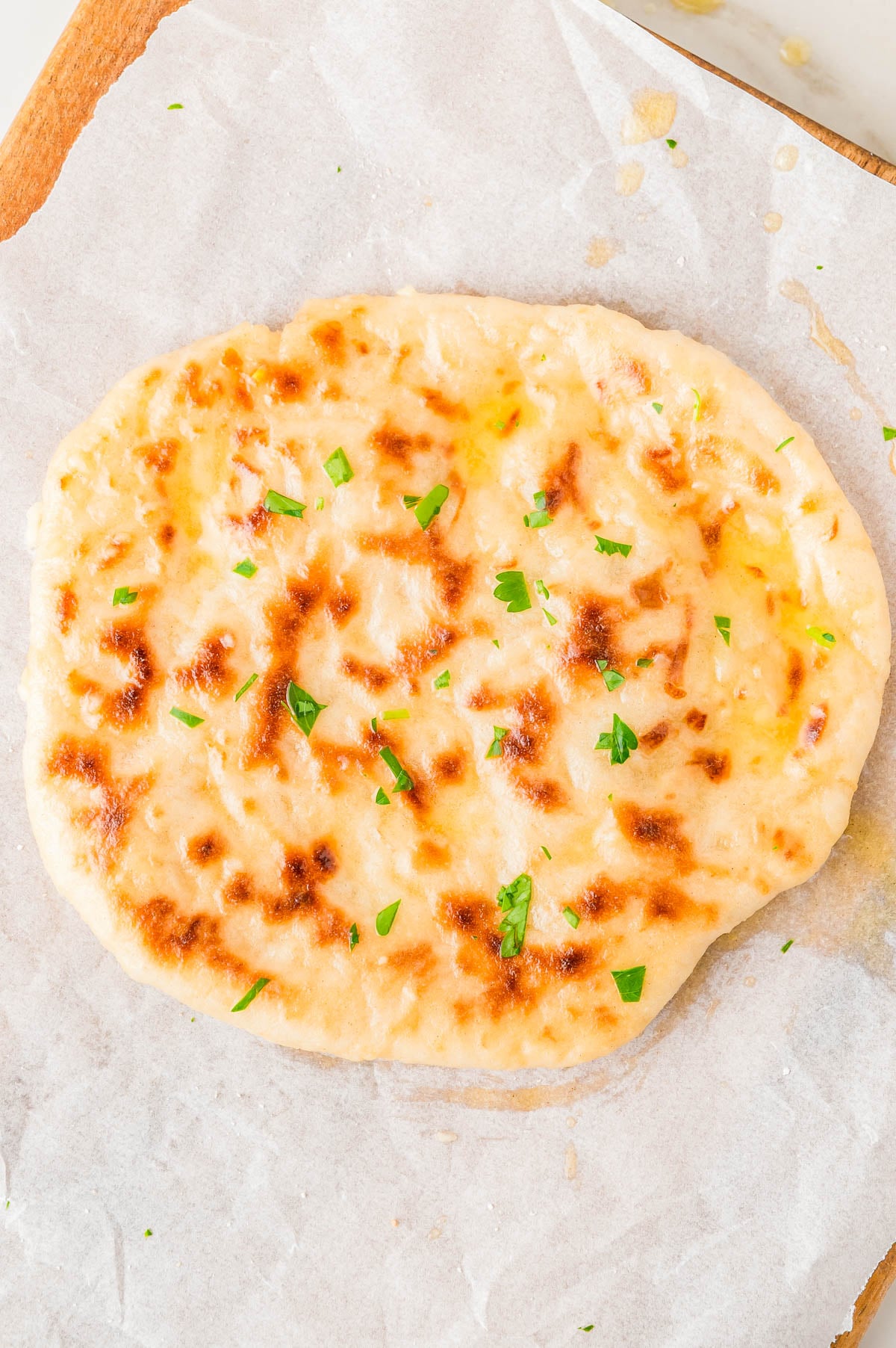 Round piece of flatbread topped with melted butter and fresh parsley on parchment paper.