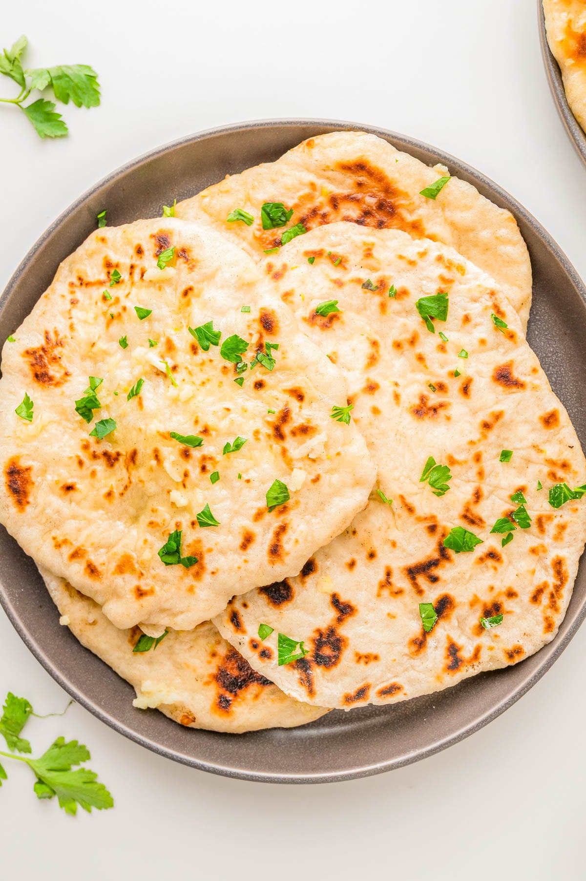 Three pieces of garlic naan topped with chopped parsley on a gray plate.