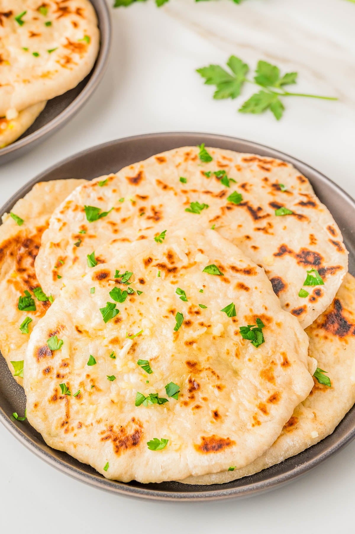A dark plate stacked with several pieces of golden-brown garlic naan garnished with fresh parsley.