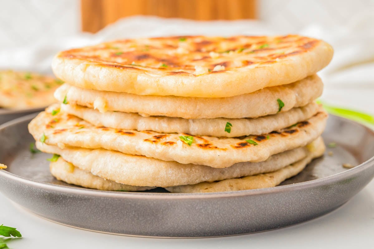 A stack of toasted flatbreads garnished with herbs on a grey plate.