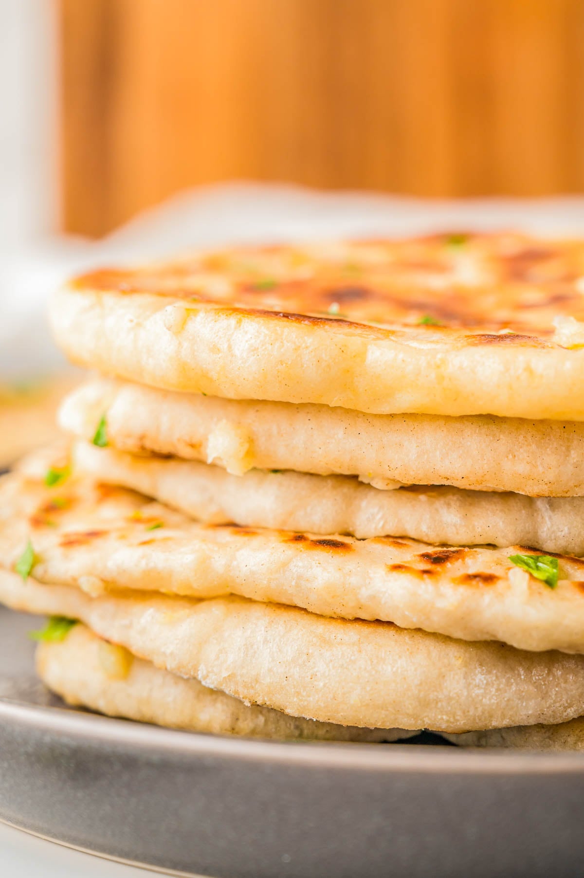 A stack of four golden-brown, pan-fried flatbreads garnished with herbs on a plate.