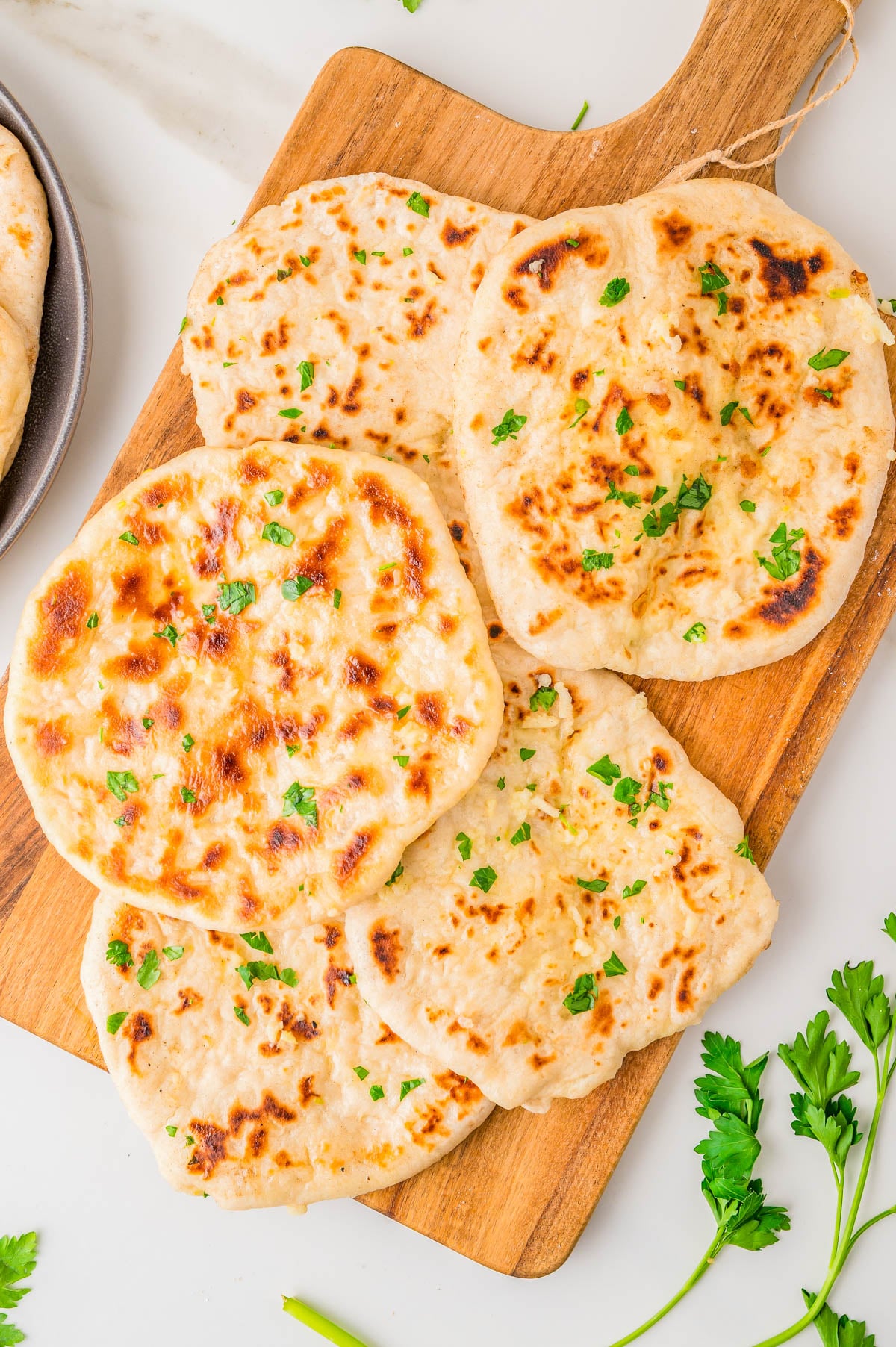 Four pieces of golden-brown garlic naan garnished with fresh parsley on a wooden serving board.