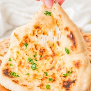A hand pulls apart a piece of garlic herb naan, showing melted cheese stretching between the two halves.