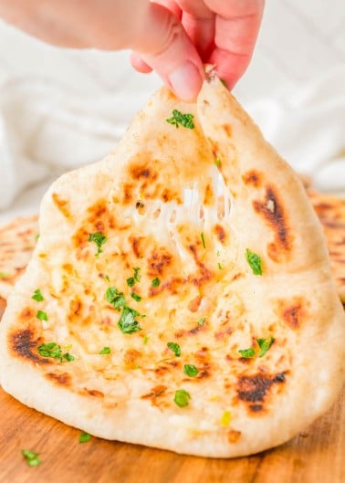 A hand pulls apart a piece of garlic herb naan, showing melted cheese stretching between the two halves.