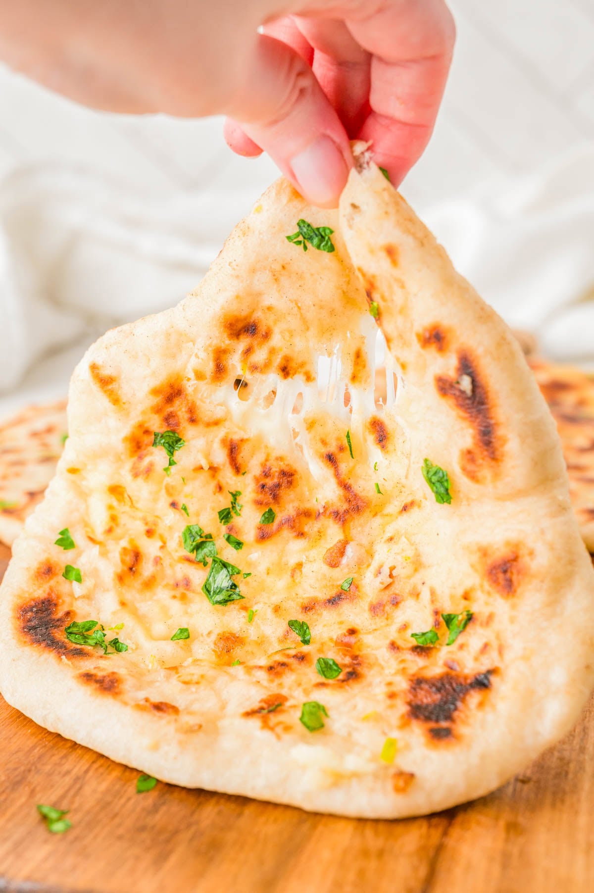 A hand pulls apart a piece of garlic herb naan, showing melted cheese stretching between the two halves.