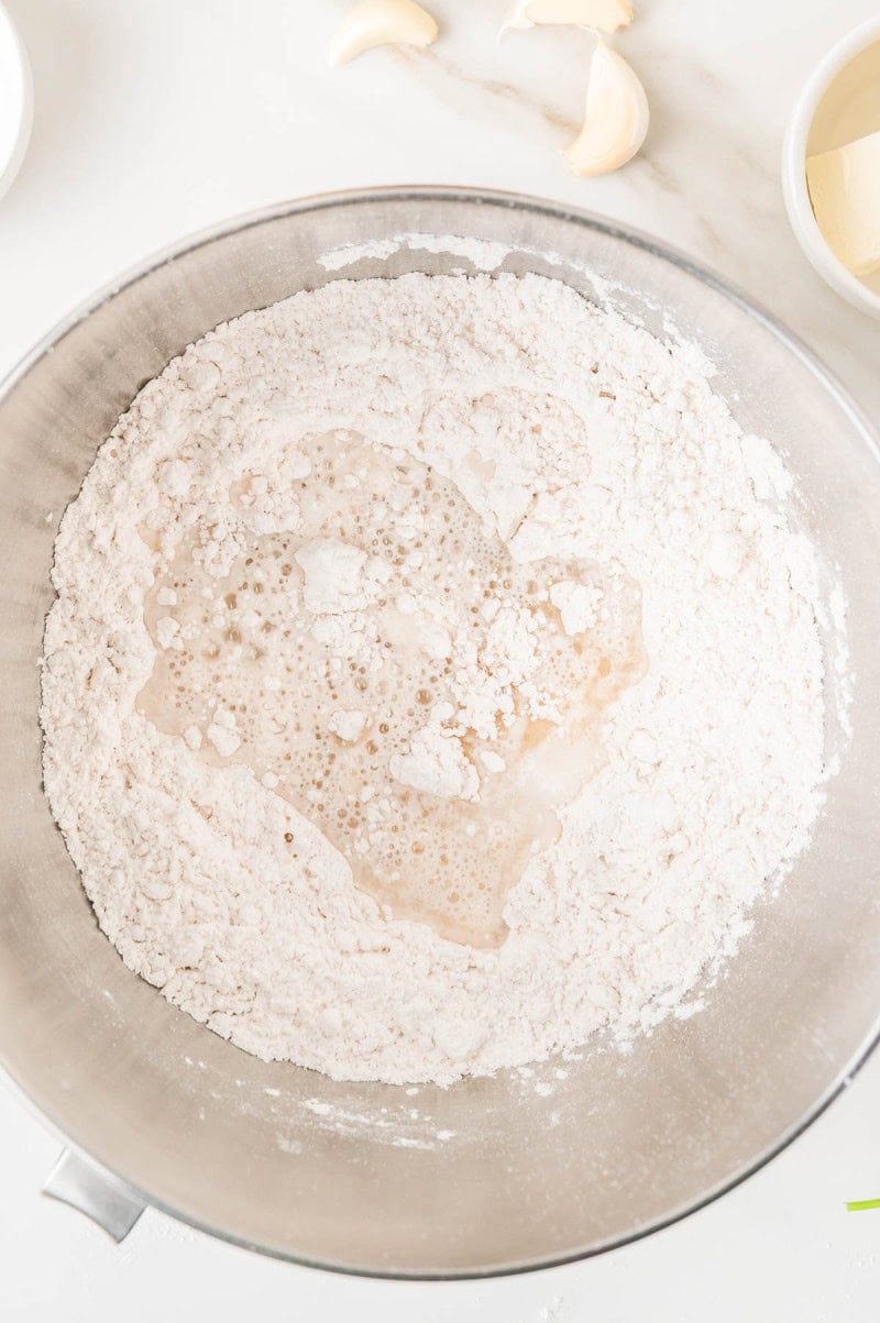 A metal mixing bowl containing flour with a pool of liquid in the center.