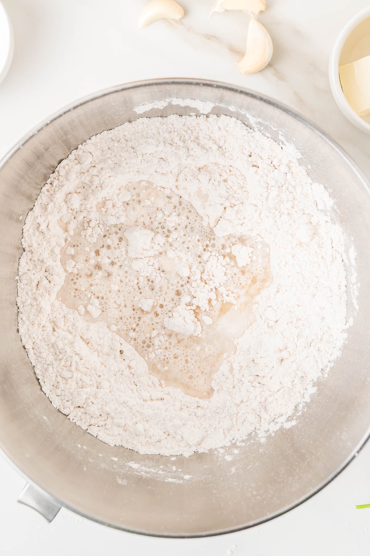 A metal mixing bowl containing flour with a pool of liquid in the center.