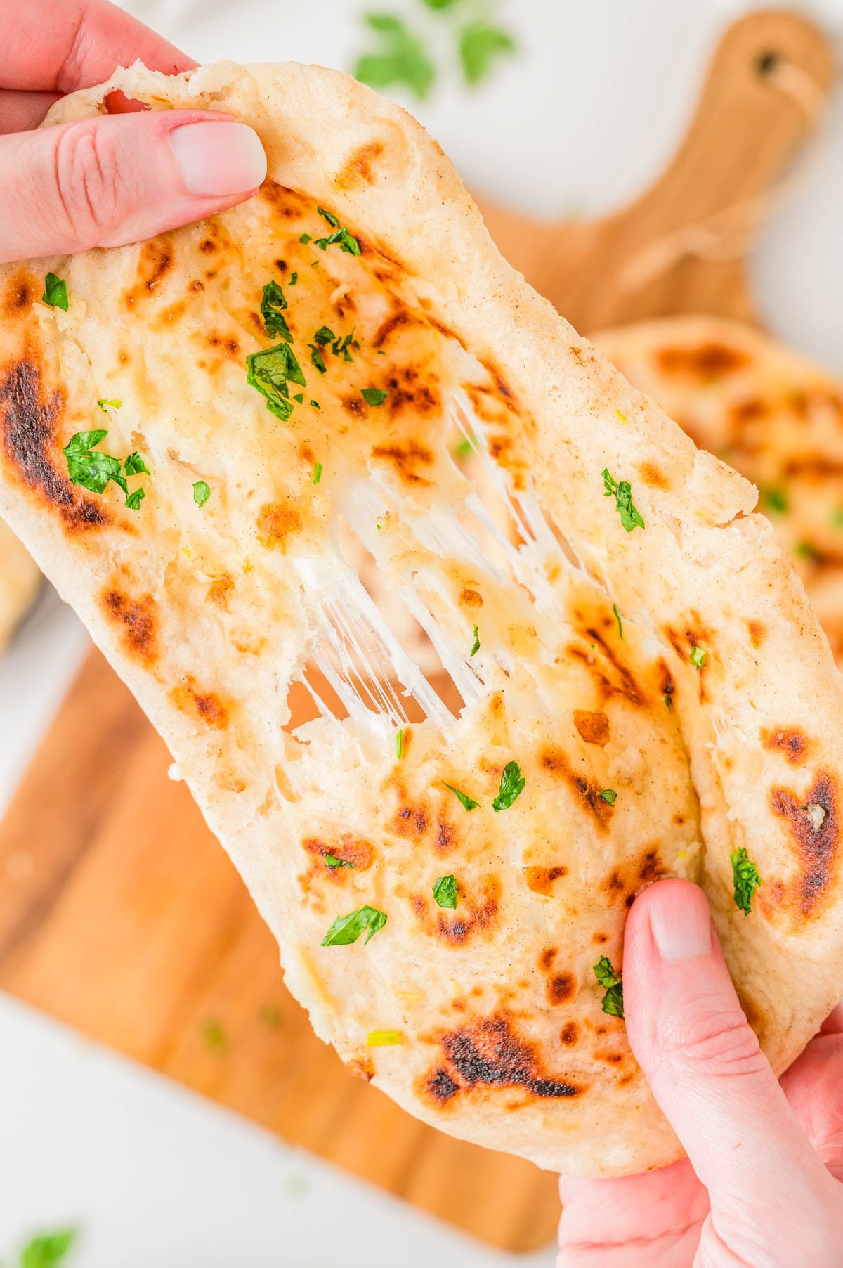 Hands pulling apart a piece of garlic herb naan with melted cheese stretching between the halves.