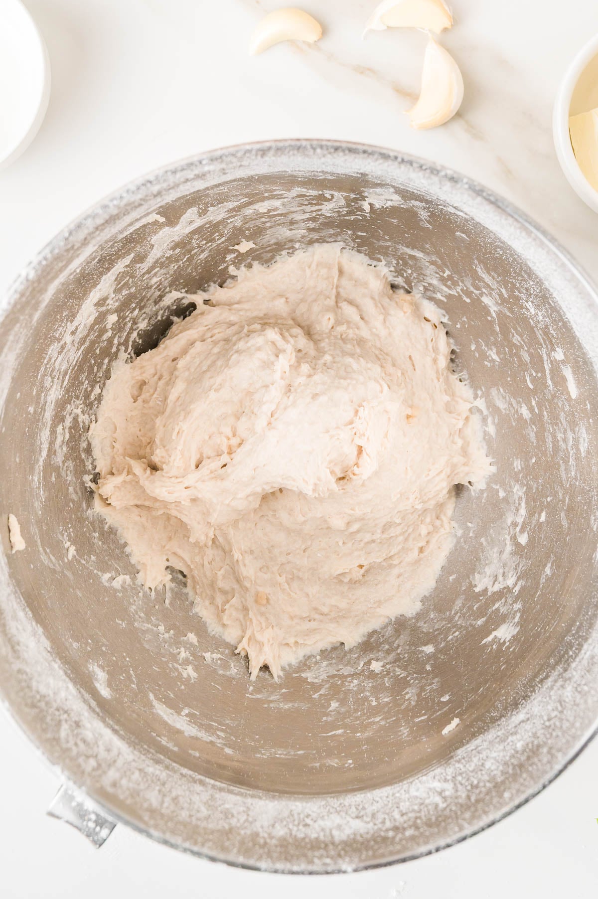 Dough in a metal mixing bowl with garlic cloves nearby.