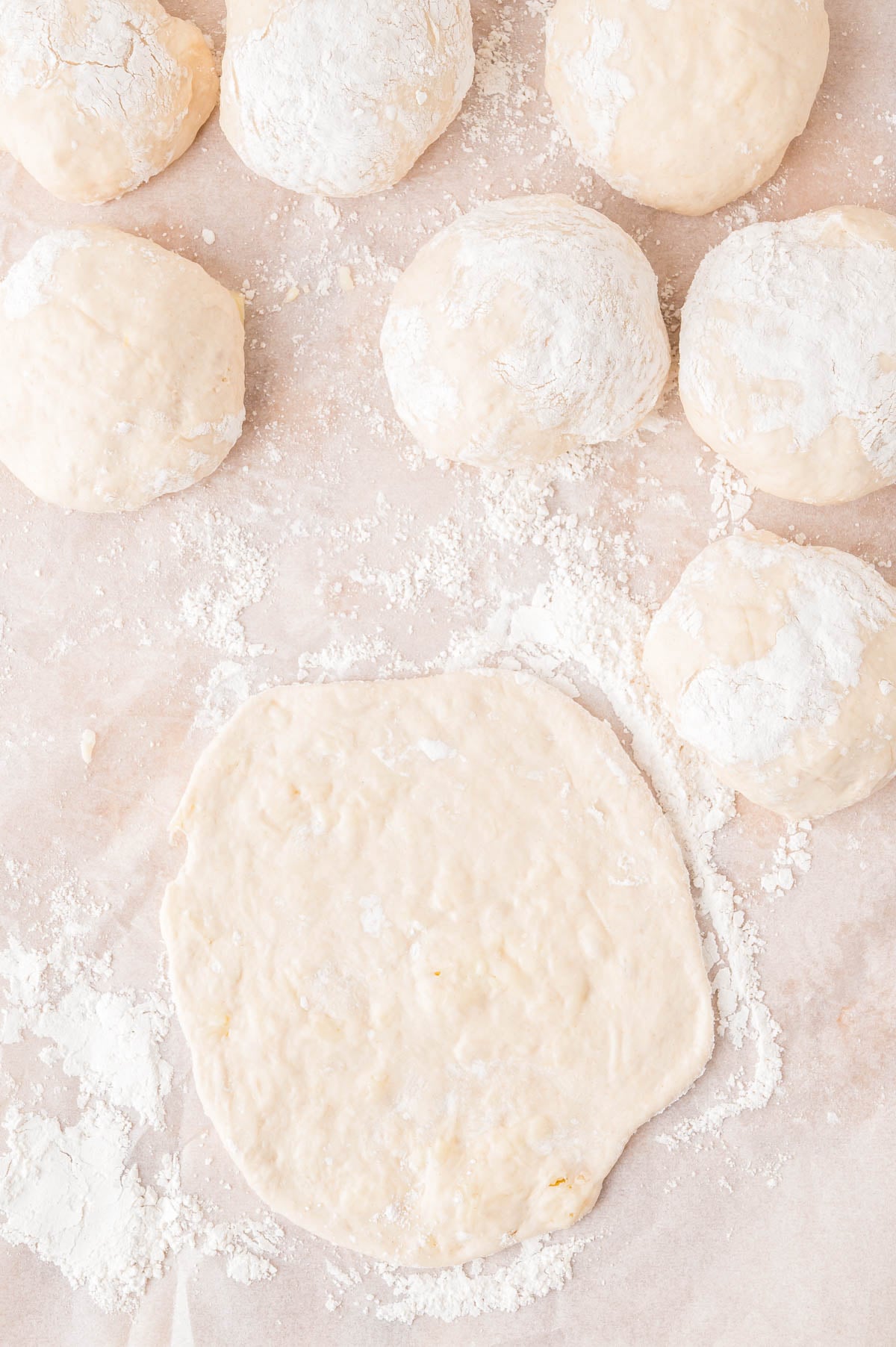 Several balls of flour-dusted dough and one flattened piece of dough on parchment paper.