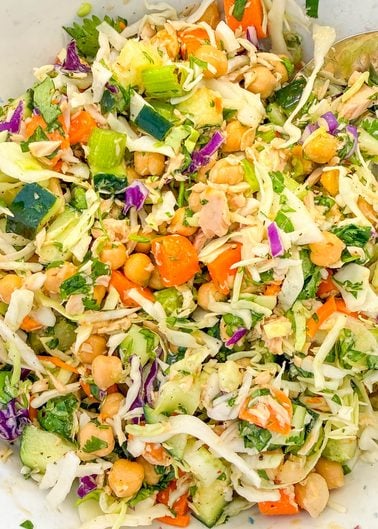 A salad of shredded cabbage, chickpeas, diced cucumber, carrots, and herbs.