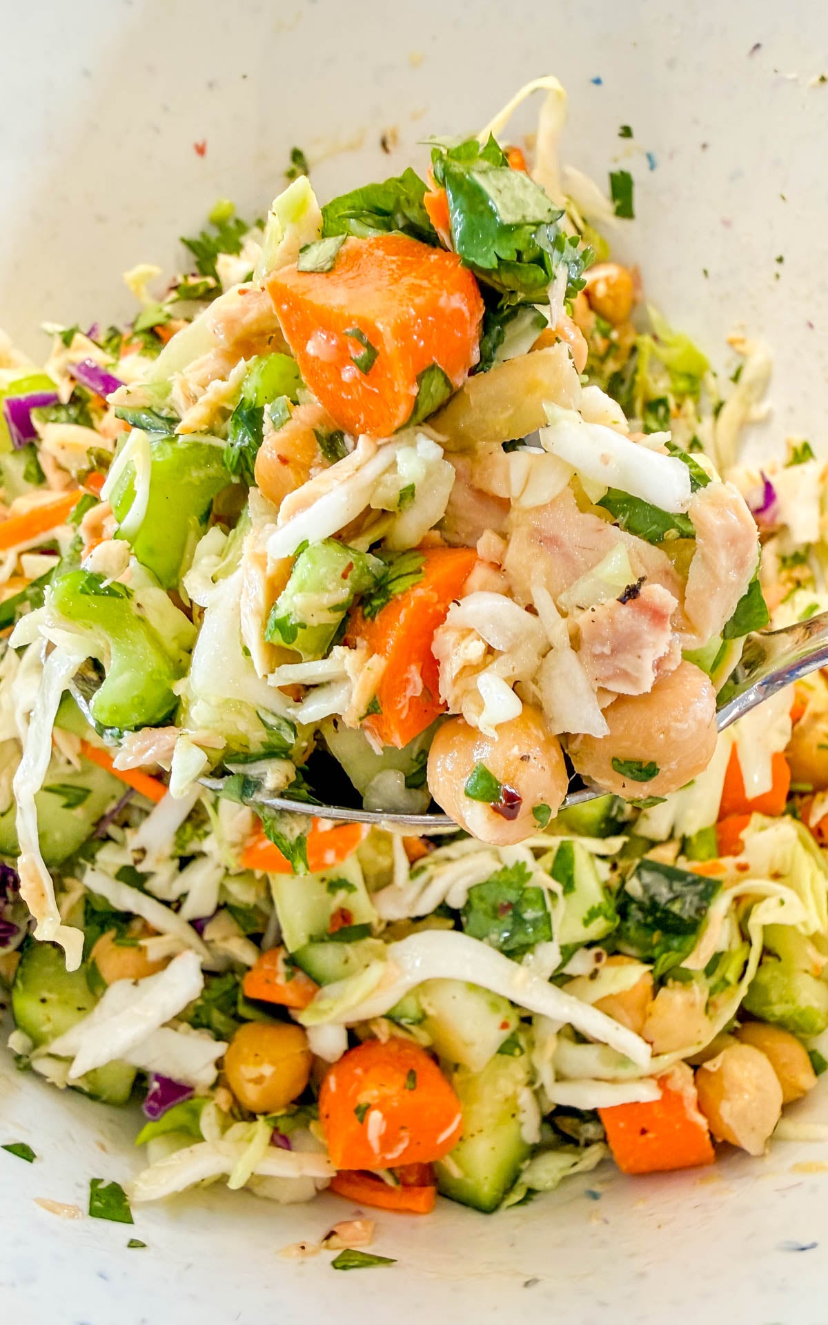 A spoonful of salad containing chickpeas, diced carrots, celery, shredded cabbage, and flaked tuna.