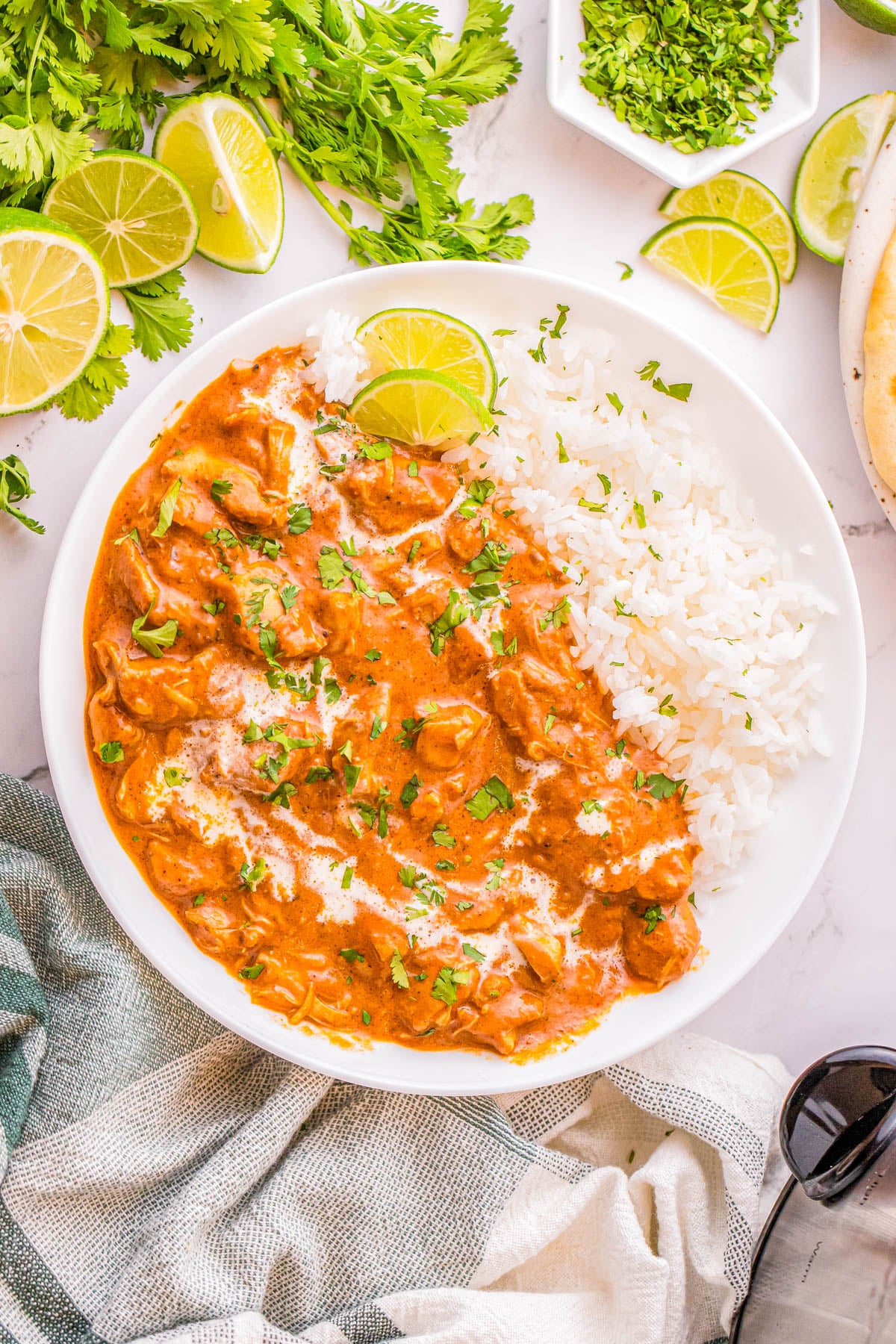 A bowl of chicken tikka masala served with white rice, garnished with fresh cilantro and lime slices.