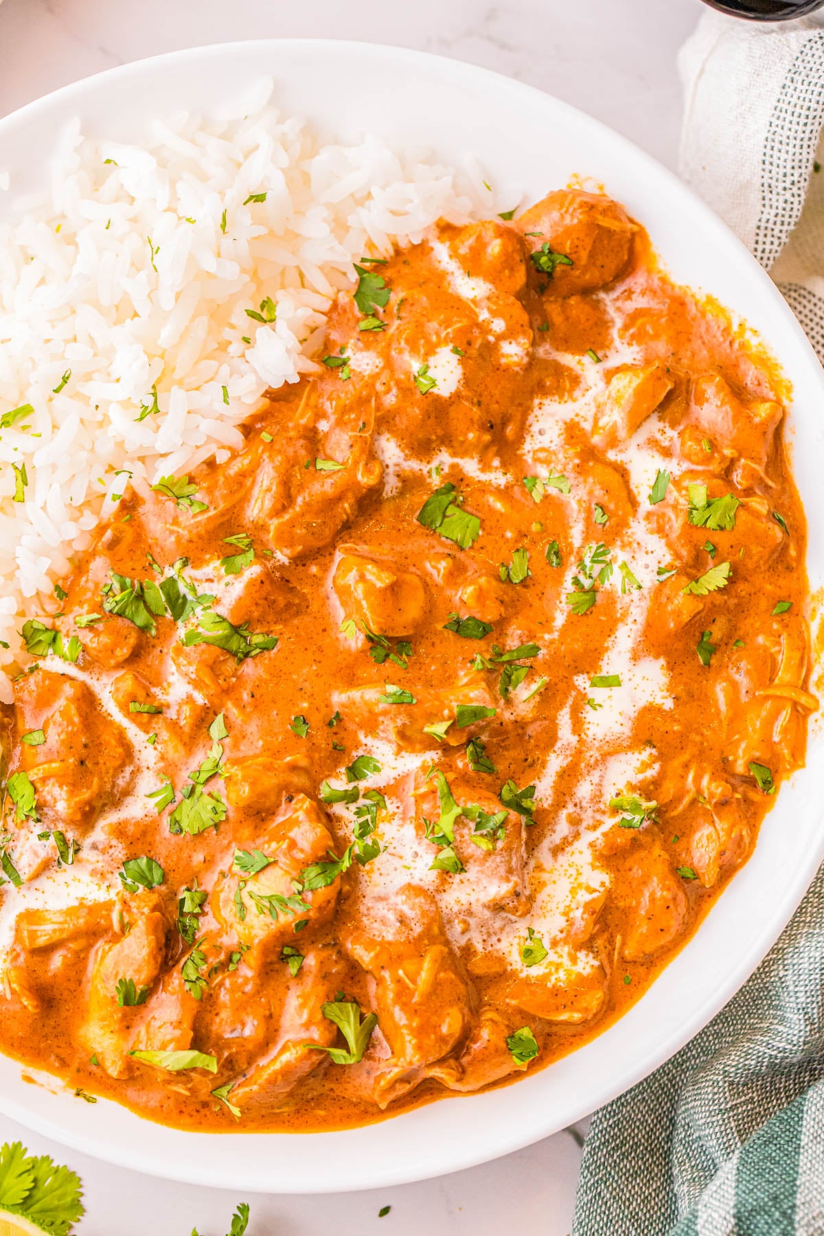 A bowl of chicken tikka masala garnished with cilantro and a drizzle of cream, served with a side of white rice.