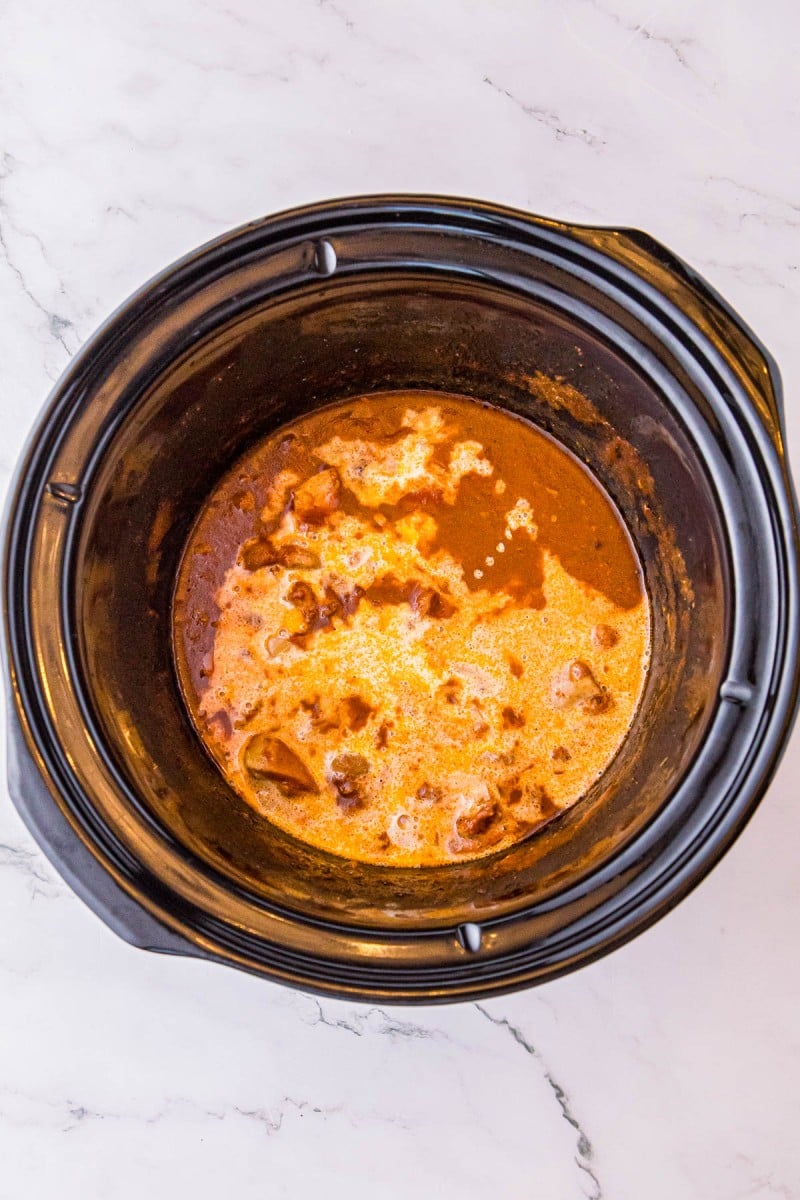 A creamy, orange-colored stew cooking in a black slow cooker insert.
