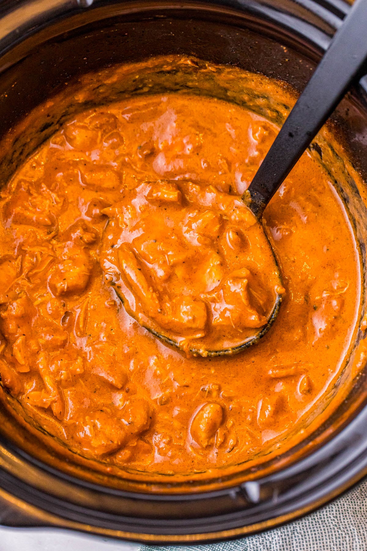 A black ladle scooping creamy orange chicken curry from a slow cooker.