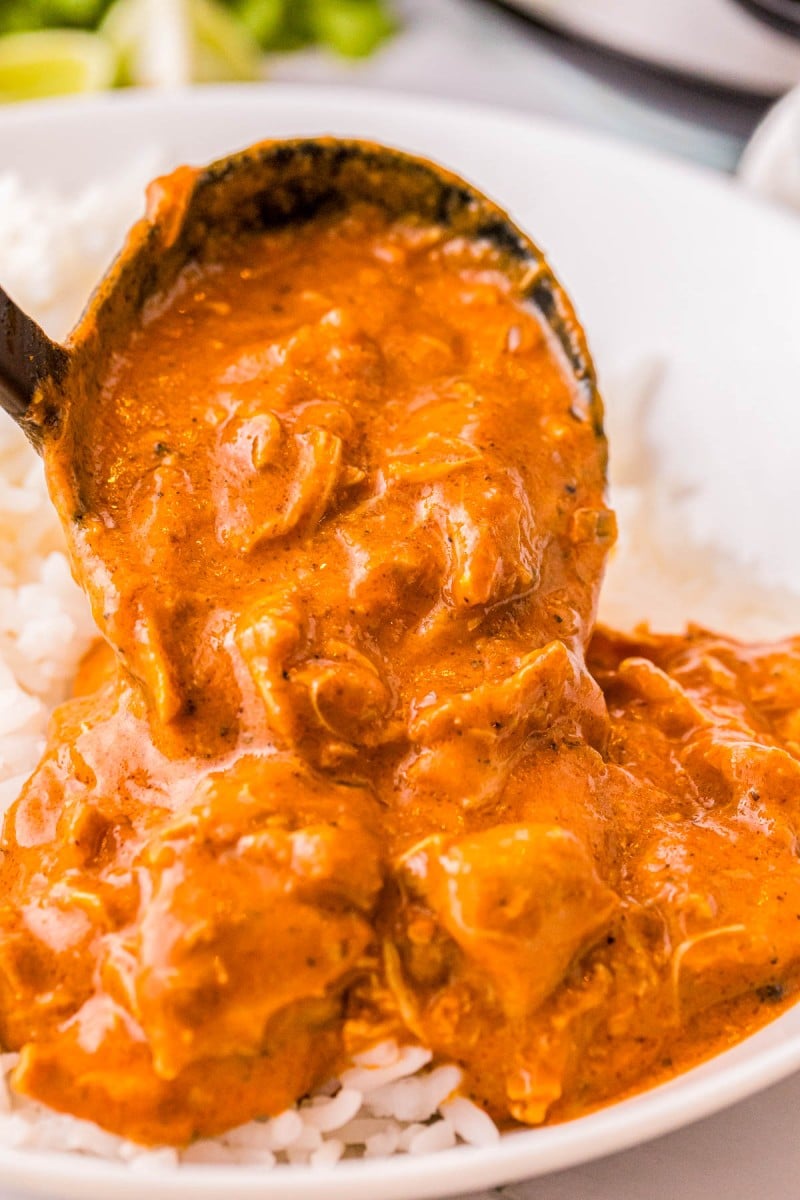 A ladle pouring chicken tikka masala over white rice.