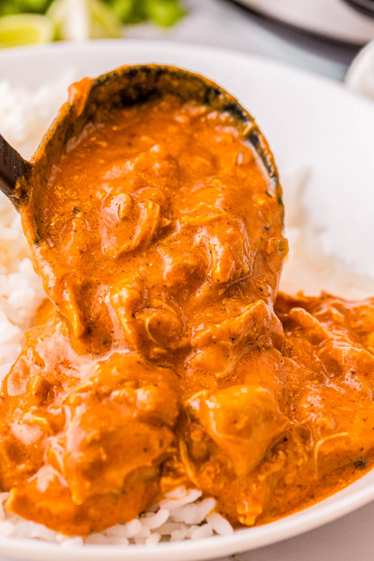 A ladle pouring chicken tikka masala over white rice.